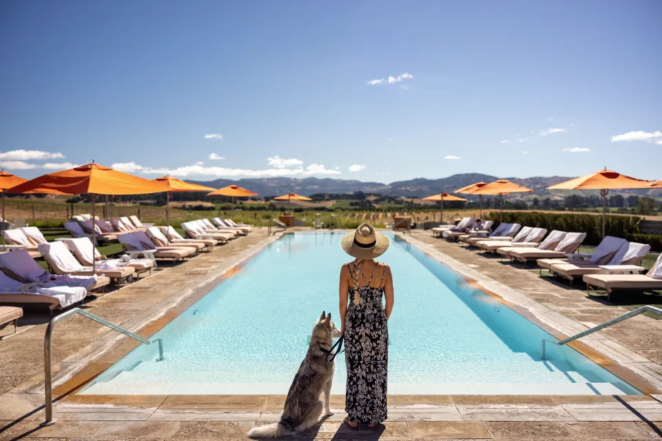 A woman in a sunhat standing at the edge of a long pool with her dog