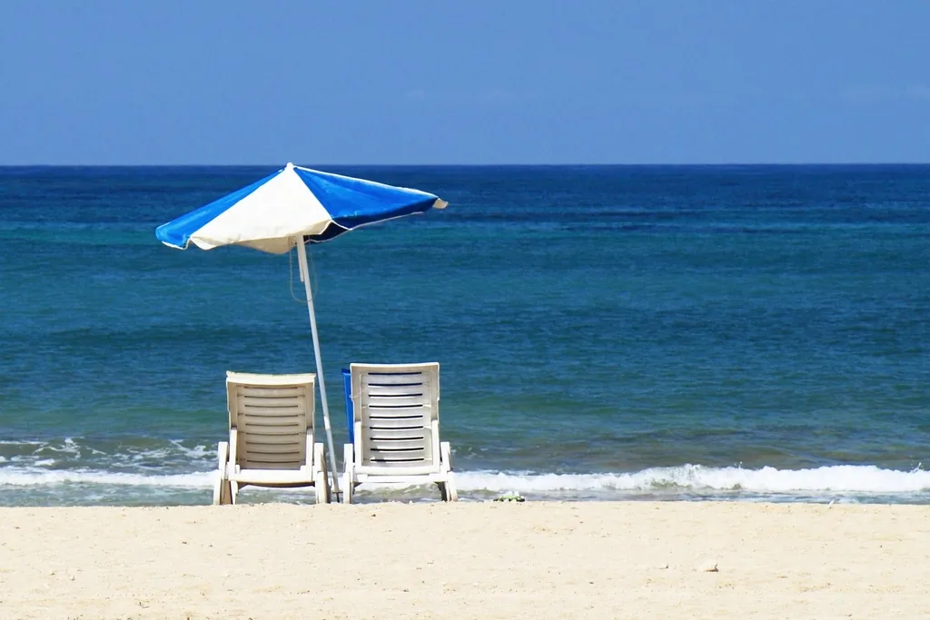 A sun umbrella and two loungers facing the open blue sea
